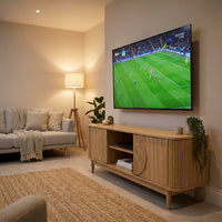 Oak TV stand styled in warm living room with wall-mounted TV above, showing open centre shelves and ribbed sliding doors