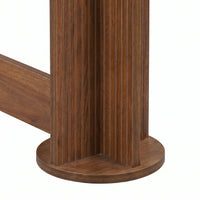 Close-up of walnut-finish console table base showing fluted cylindrical pedestal leg on circular disc foot with stretcher…