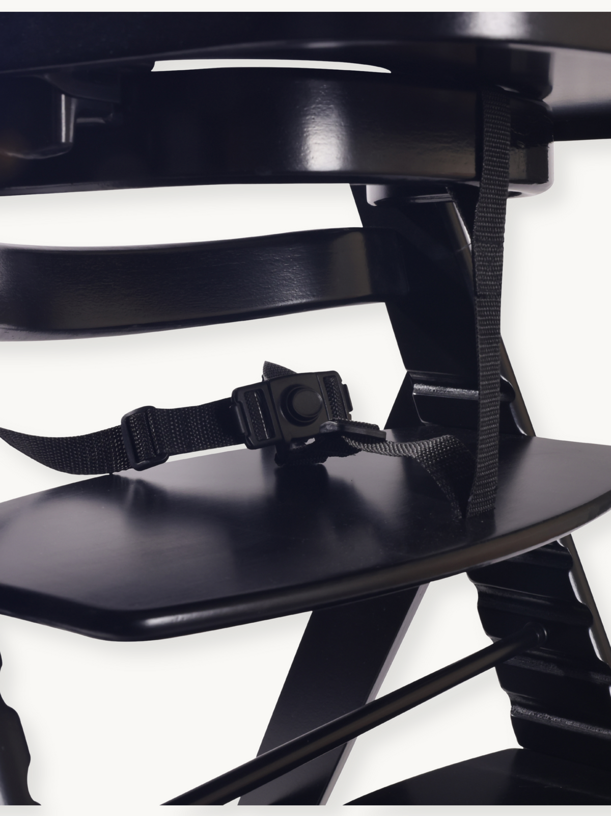 Close-up of black highchair seat showing black buckle safety harness and adjustable webbing straps resting on the fitted tray