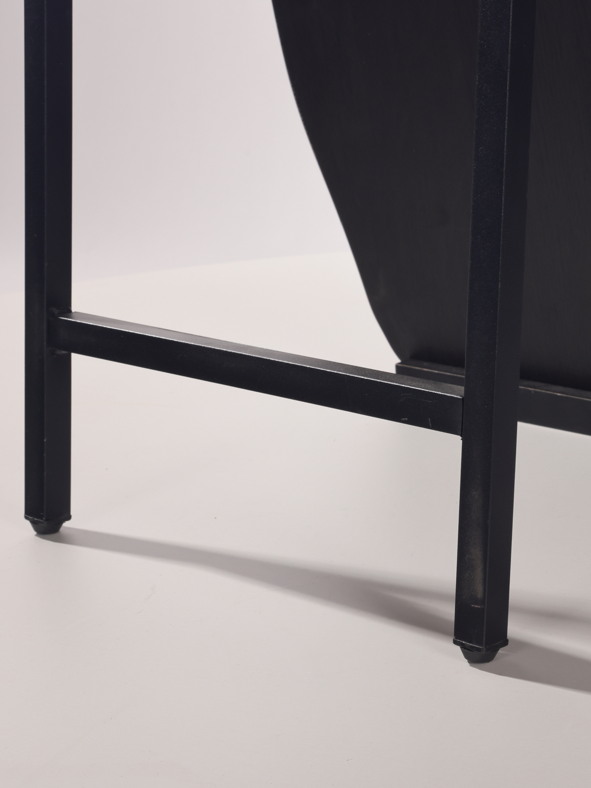 Close-up of black wooden frame base showing two square legs joined by a horizontal stretcher with small rubber feet