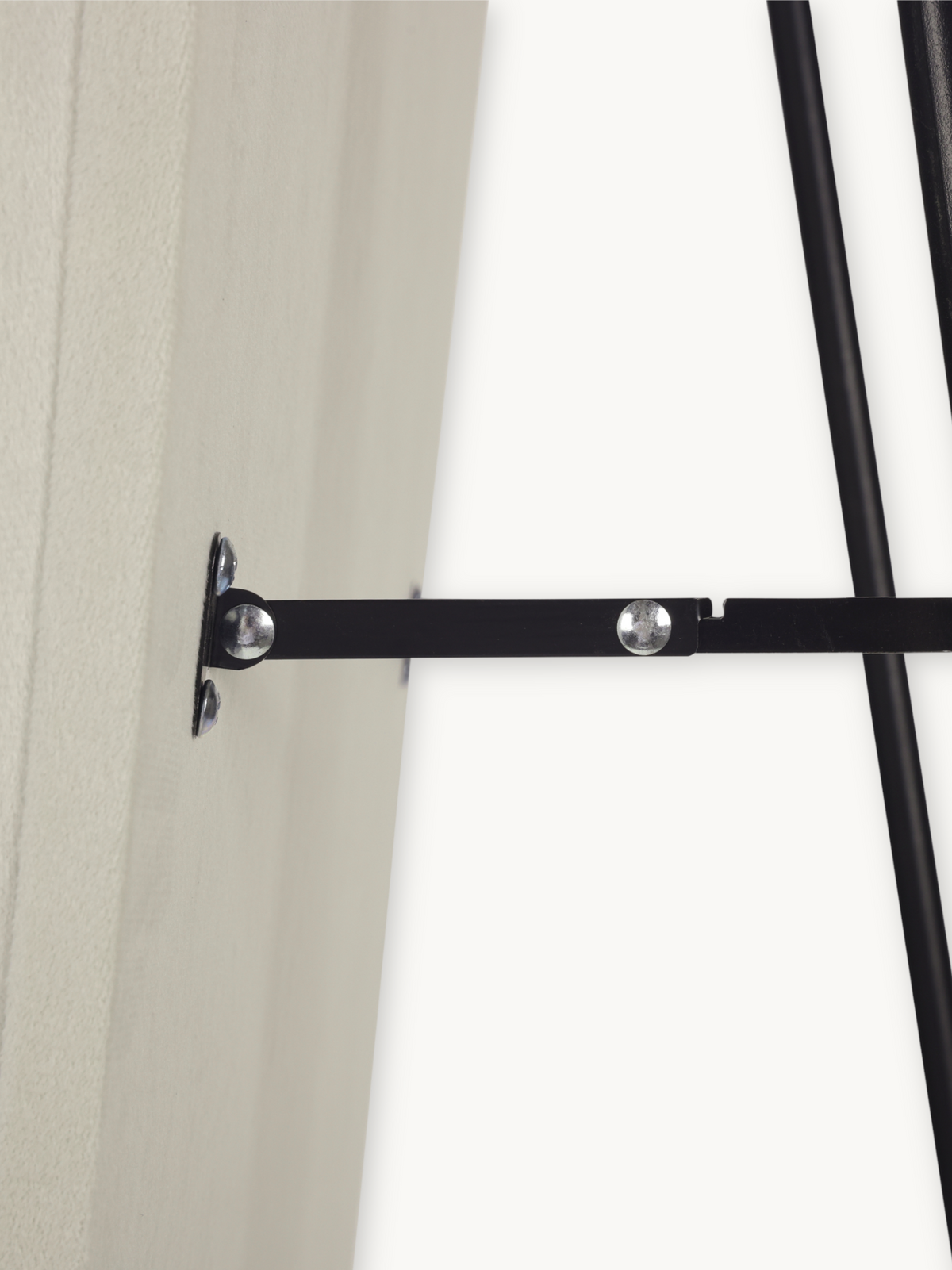 Close-up of black metal flat bar connecting mirror frame to wall-mounted bracket, showing silver rivet fixings and rod joints