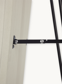 Close-up of black metal flat bar connecting mirror frame to wall-mounted bracket, showing silver rivet fixings and rod joints