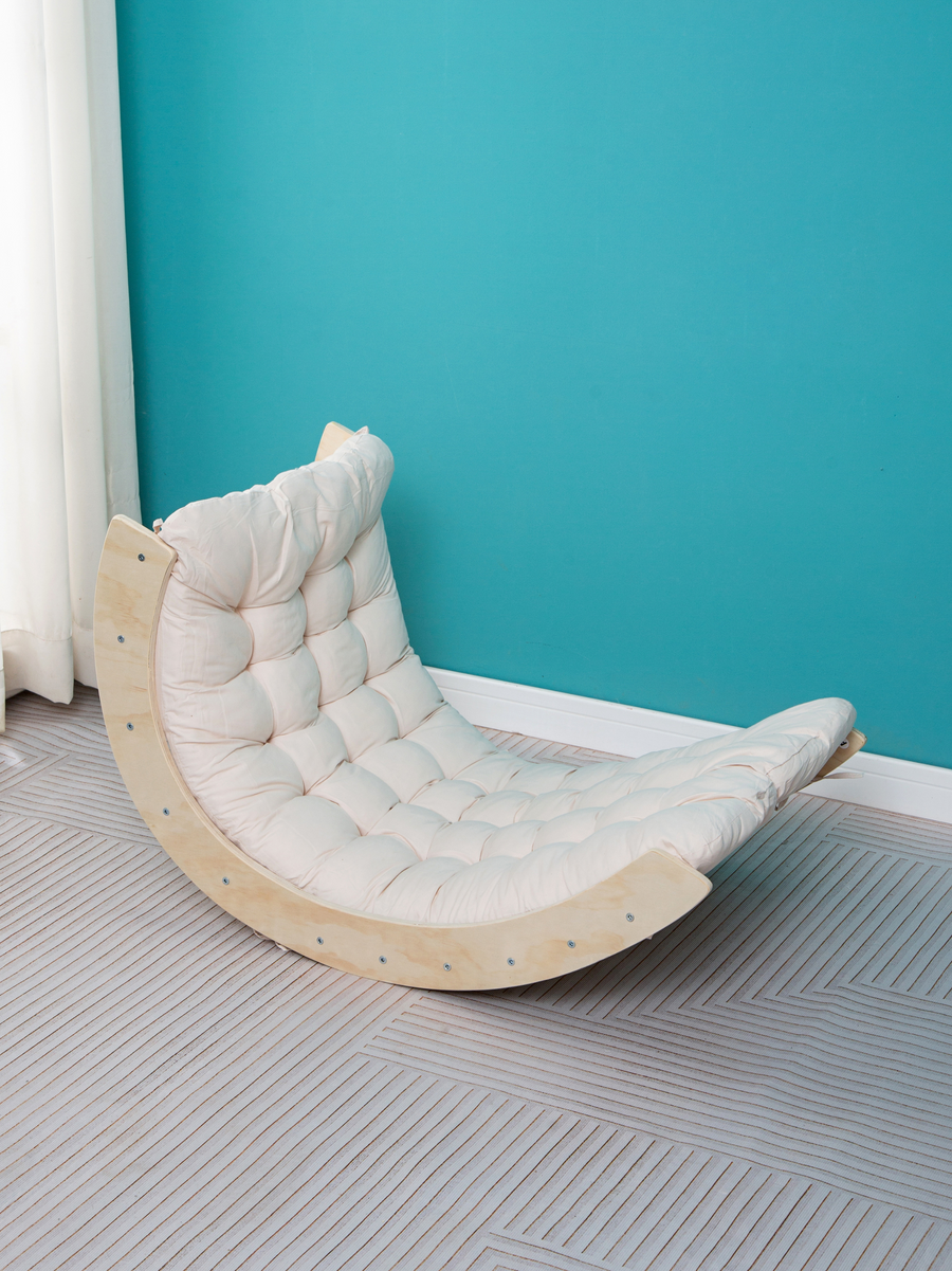 Curved pine climbing arch rocker with cream tufted cushion, lifestyle shot against teal wall on herringbone floor