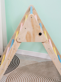 Close-up of birch plywood side panel and black star knob fastener on a pastel-rung Pikler triangle, mint wall behind