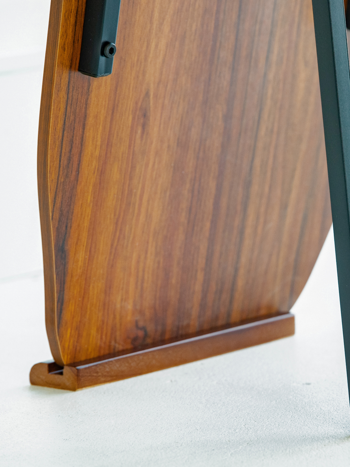 Close-up of walnut-finish wooden base and lower frame detail of asymmetric standing mirror with black metal hardware