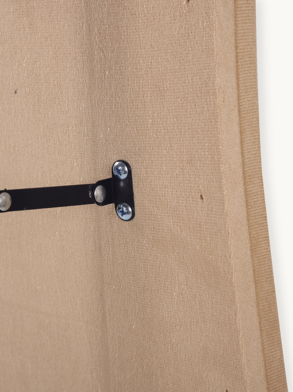Close-up of black metal T-bracket with silver screws securing the stand to the taupe suede velvet-covered back panel of th…