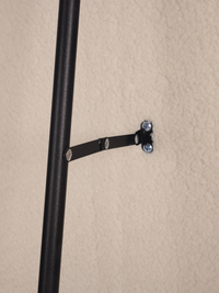 Black metal wall bracket securing the mirror's support pole to a textured cream wall, close-up installation detail