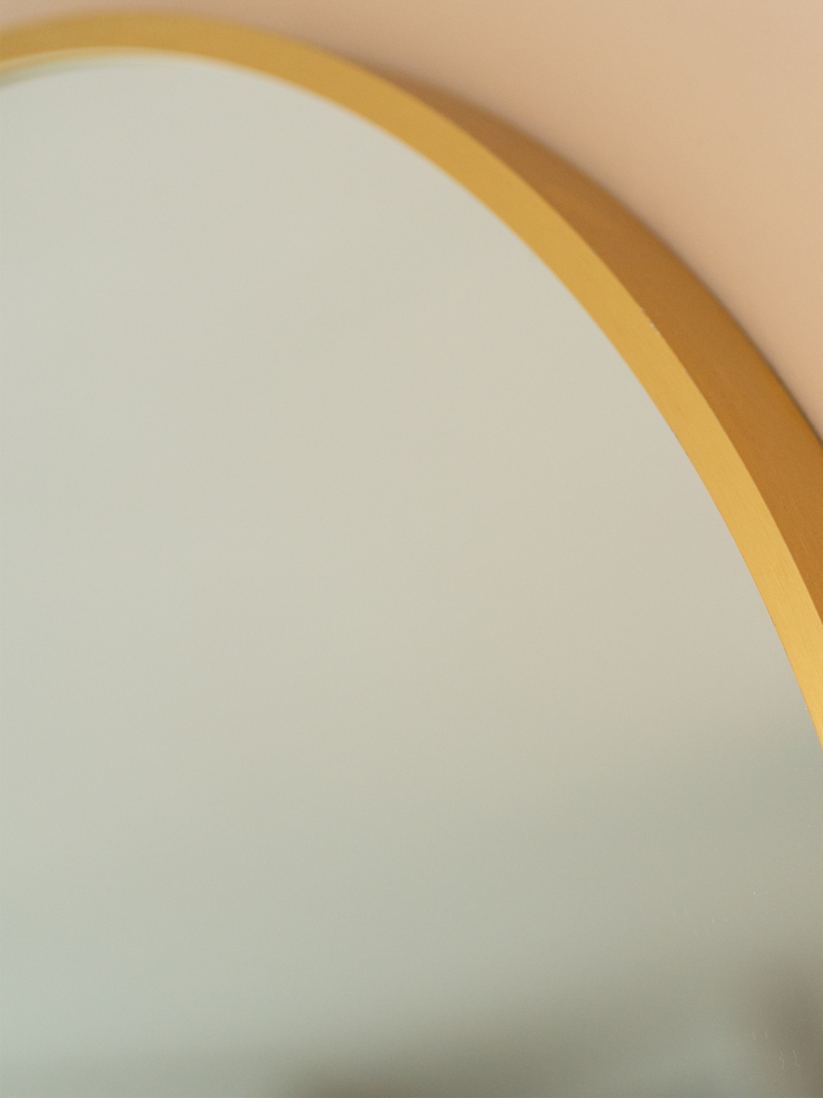 Close-up of gold metal rim and upper-left arc of round Freya mirror against a blush pink wall
