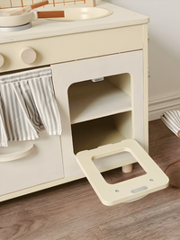 Cream wooden play kitchen oven compartment open, door lying flat on wood floor, revealing two interior shelves