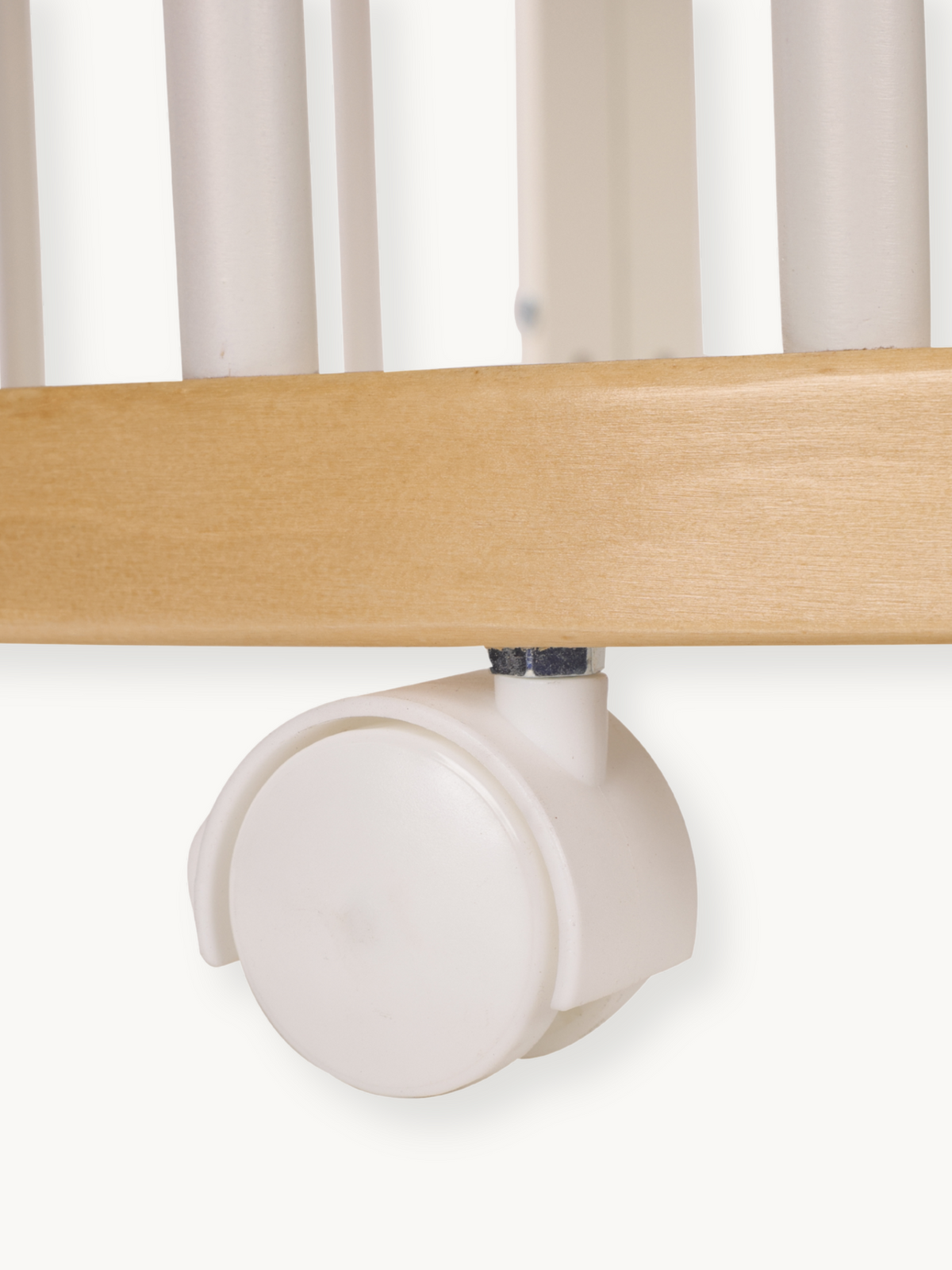 Close-up of a single cream plastic twin-wheel castor fitted to the natural wood base rail of a baby playpen