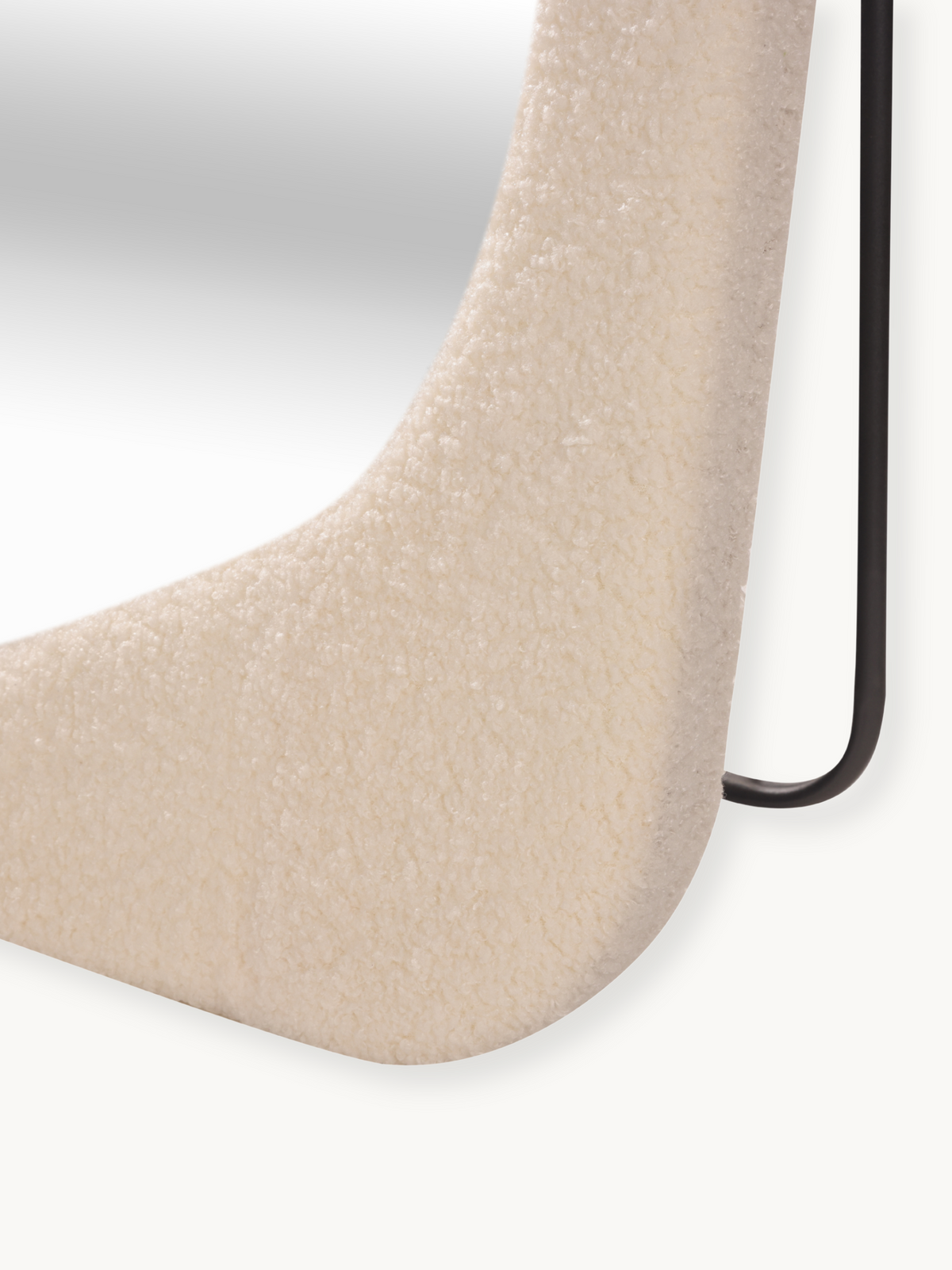Close-up of cream white bouclé teddy fabric upholstery on the lower curve of the Felis mirror frame, black metal leg visible