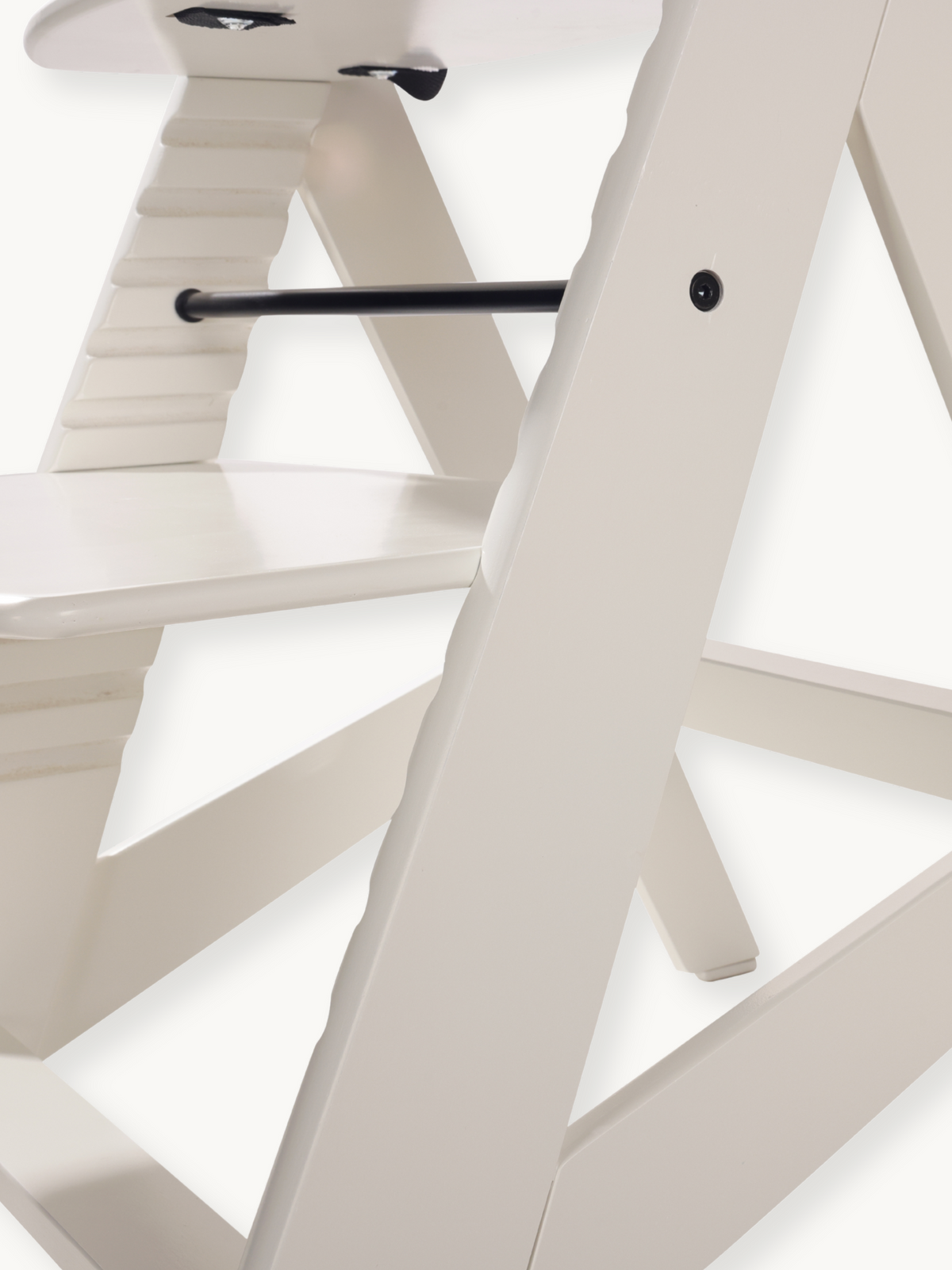Close-up of white wooden high chair cross-brace legs and black metal footrest bar with visible bolt detail