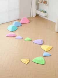 11 pastel balance stepping stones arranged in a curved path on a herringbone wood floor, children's bookshelf visible in b…