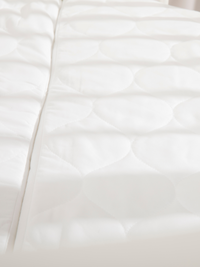 Close-up of white quilted mattress surface showing circular embossed pattern, with playpen side rail visible at left edge