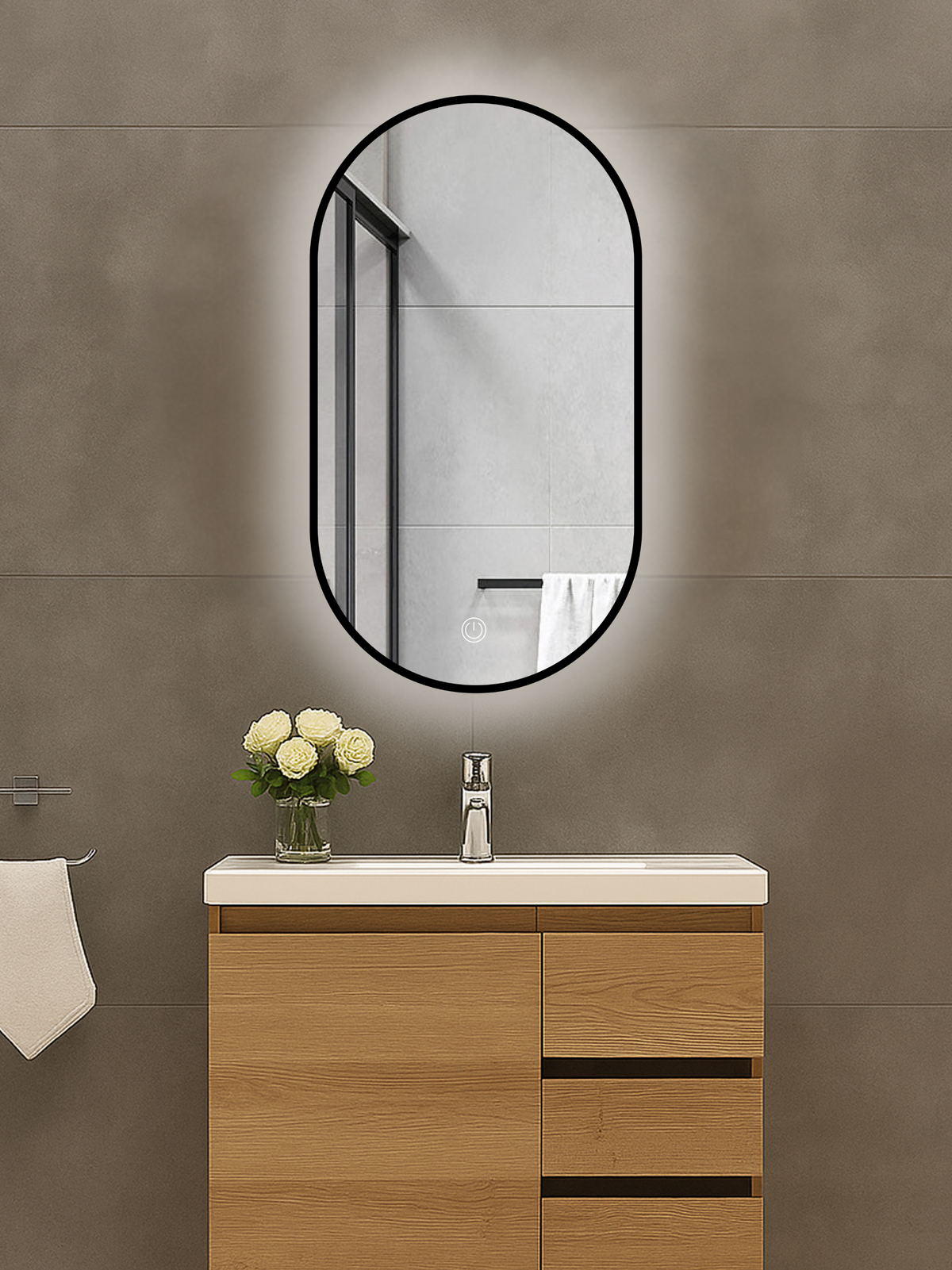 Oval black-framed LED mirror mounted above a wood vanity unit, glowing backlight visible against grey tiled wall, touch co…
