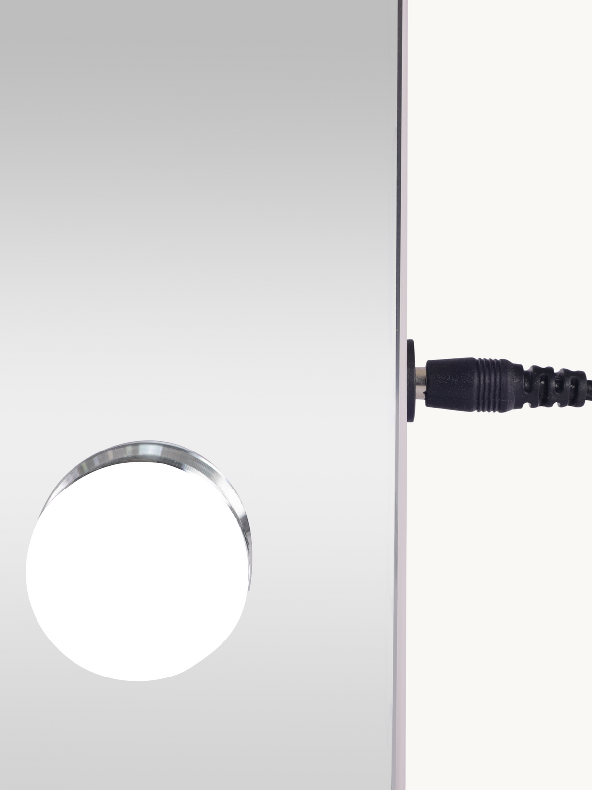 Close-up of a single round LED bulb on the mirror surface and black DC power cable connector on the white frame edge