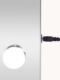 Close-up of a single round LED bulb on the mirror surface and black DC power cable connector on the white frame edge