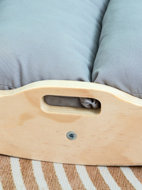 Close-up of natural plywood carry handle cutout and visible screw on the side panel of a wooden climbing arch, grey cushio…