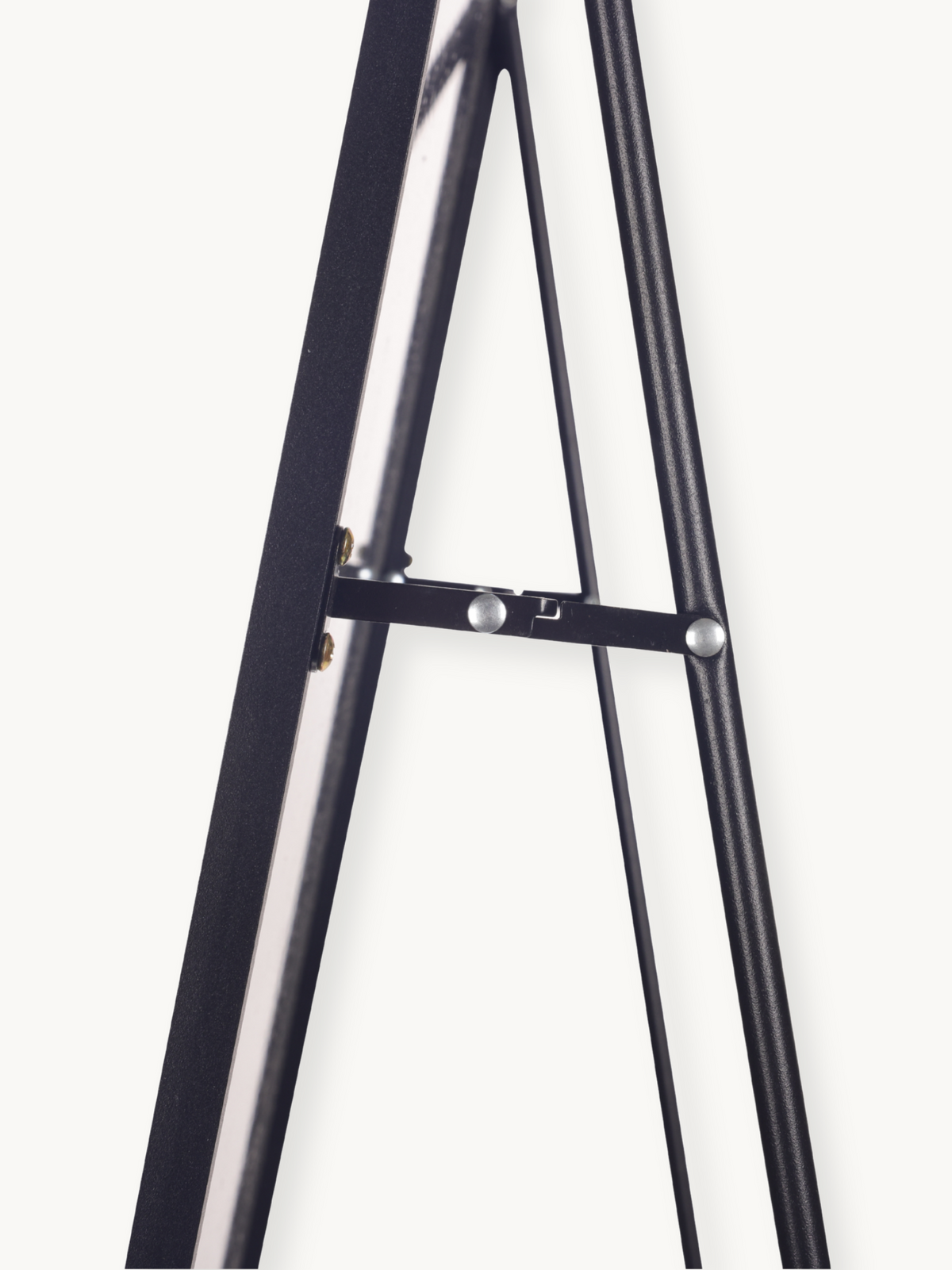 Close-up of black aluminium easel-style mirror stand showing hinged spreader bar with silver rivets and brass adjustment h…