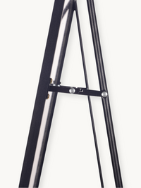 Close-up of black aluminium easel-style mirror stand showing hinged spreader bar with silver rivets and brass adjustment h…