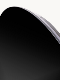 Close-up of the upper-right curved edge of a round frameless mirror, showing 5 mm black-tinted glass thickness and clear rim