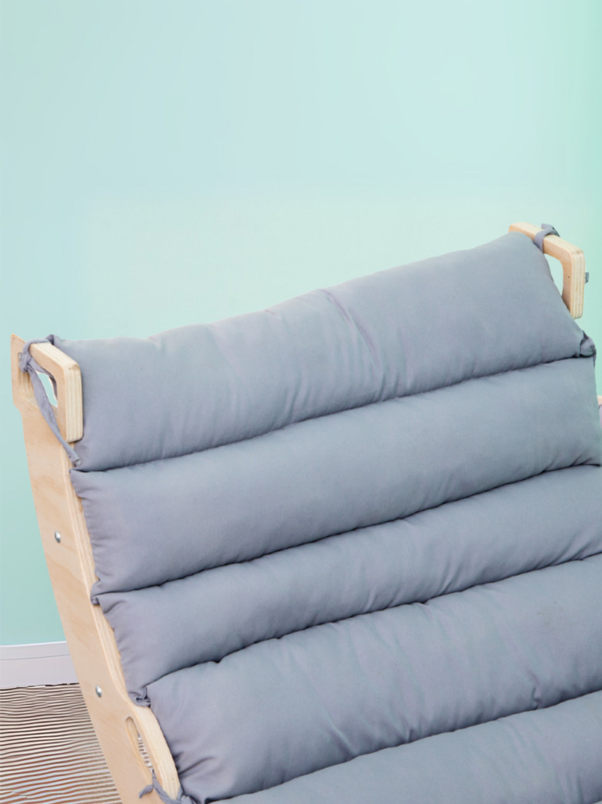 Close-up of grey channel-stitched cushion tied onto natural wood climbing arch backrest, mint green background