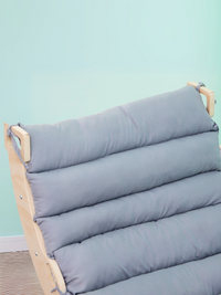 Close-up of grey channel-stitched cushion tied onto natural wood climbing arch backrest, mint green background