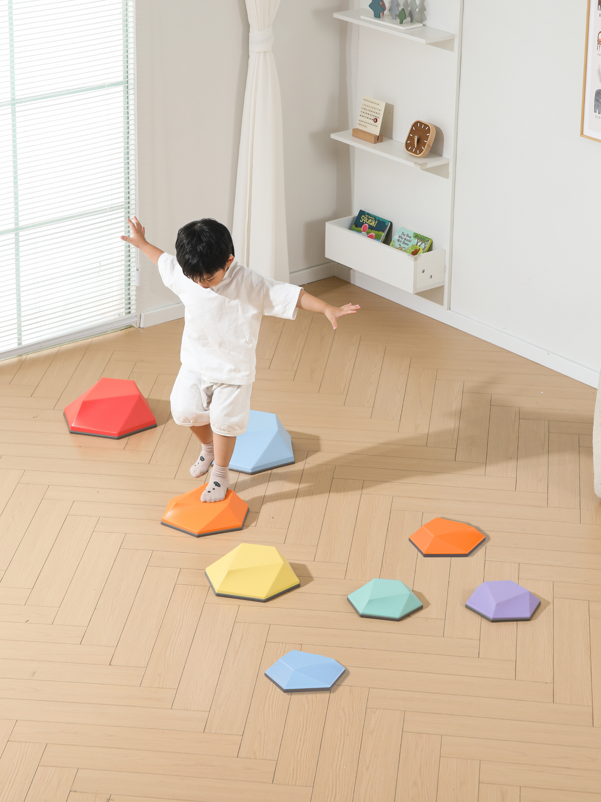 Young boy balancing arms outstretched while hopping across colourful hexagonal stepping stones spread across a light wood…