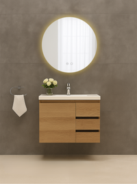 Round LED backlit bathroom mirror mounted above a wall-hung oak vanity unit with white basin, warm glow visible around mir…