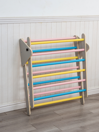 Climbing arch with pink, yellow, and blue rungs leaning against white panelled wall, grey wooden side panels, folded flat