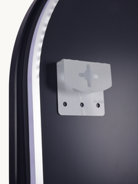 Close-up of translucent plastic wall-mounting bracket with cross-slot and three screw holes, against dark mirror back surf…