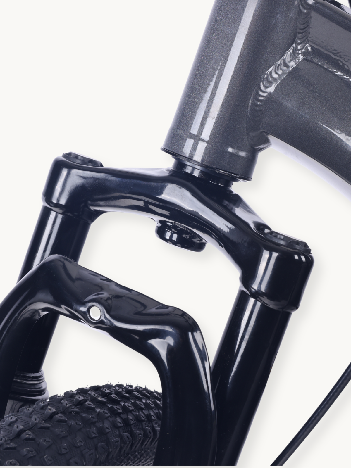 Close-up of black front suspension fork crown and steerer tube junction, with knobby tyre visible below on grey steel frame