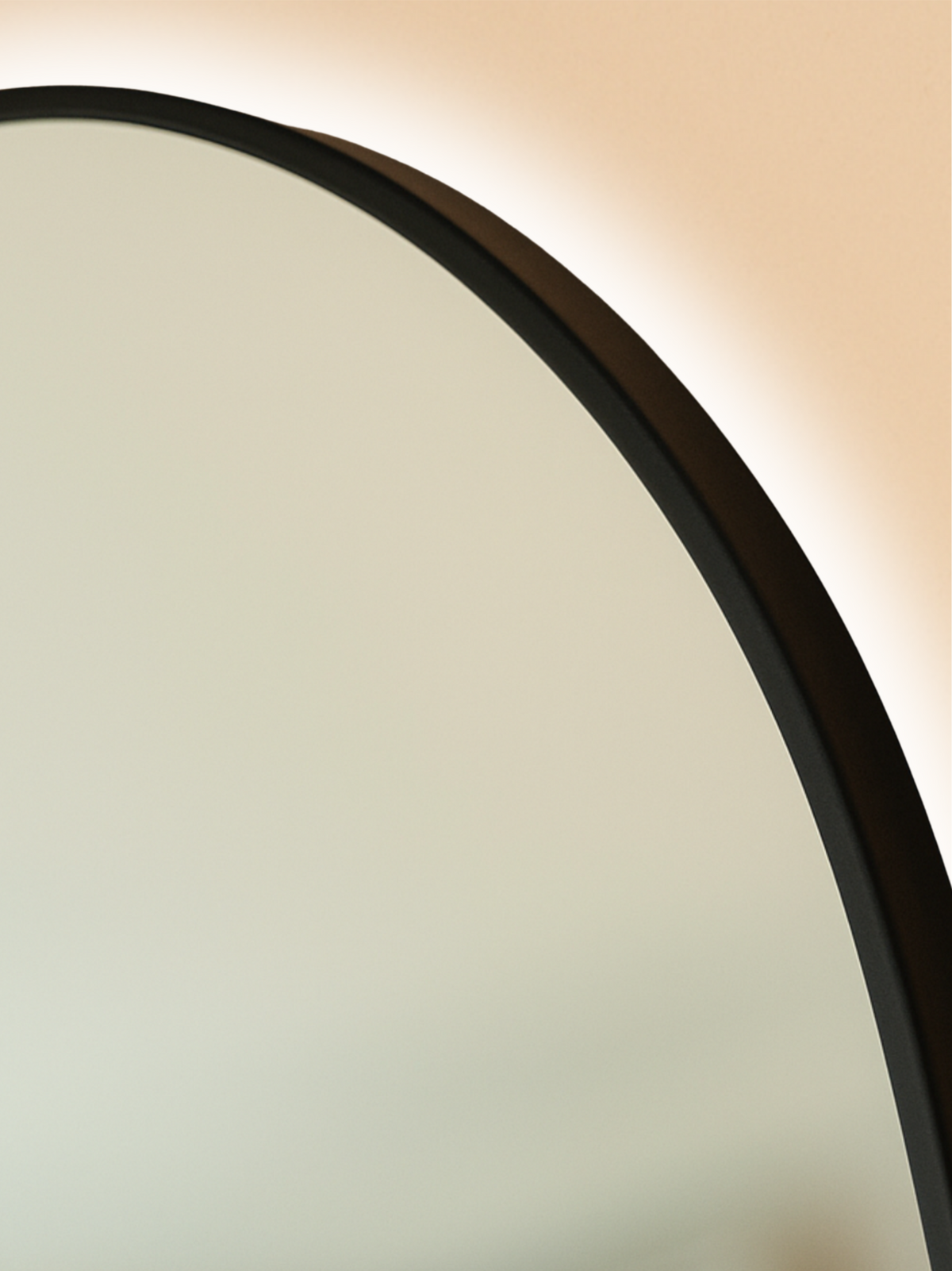 Close-up of upper curve of oval mirror showing matte black metal frame edge and warm LED backlight glow against beige wall