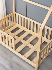 Overhead angle showing natural pine slatted base and screw fixings inside children's house bed frame, no mattress, grey wa…