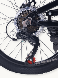 Close-up of Shimano Tourney TZ rear derailleur with red jockey wheel, 6-speed cassette, chain, and perforated disc rotor o…