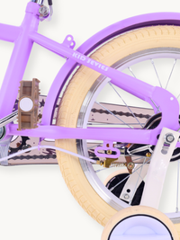 Close-up of purple Kid Series frame, cream rubber tyre, chrome spokes, chain, brown pedal, and stabiliser wheel detail