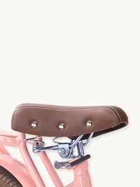 Brown leather-look saddle with silver studs and white stitching on pink children's bike frame, chrome spring suspension de…