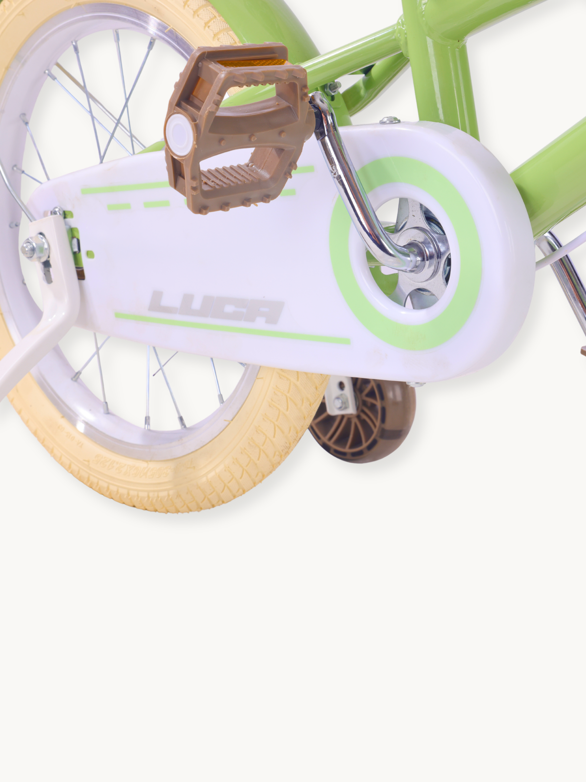 Close-up of Luca children's bike drivetrain area showing white chain guard, brown pedal, cream tyre, and green training wheel
