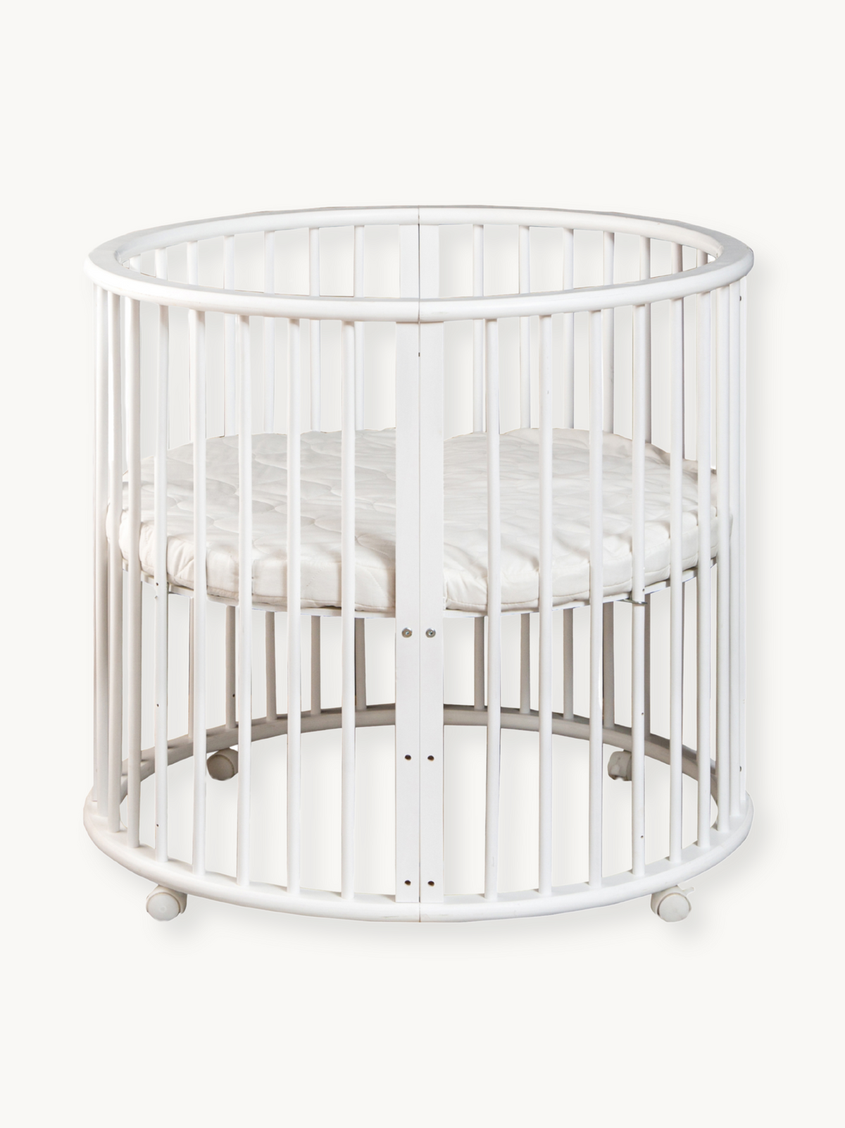 White round wooden baby playpen with vertical slats, oval top rail, fitted mattress, and four rolling casters, front view…