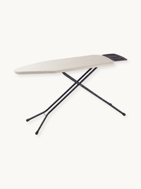 Taupe cotton-covered ironing board with black steel cross-frame legs and dark iron rest holder, angled product view on whi…
