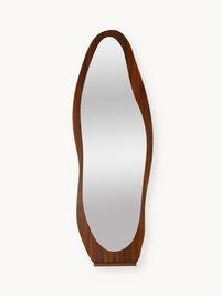 Tall asymmetric full-length mirror with warm brown wood grain frame, organic curved silhouette, front view on white backgr…