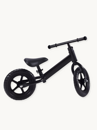 Matte black children's balance bike, angled three-quarter view, showing five-spoke wheels, padded saddle, and rubber tyres