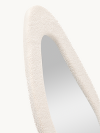 Close-up of Seraphina mirror's curved teddy fabric frame top, showing off-white bouclé texture and oval cutout detail