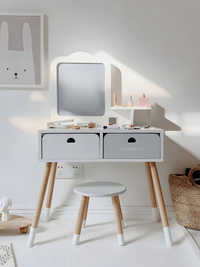 White children's wooden vanity set in bright nursery, front view showing two drawers, square mirror, stool, and pastel toy…