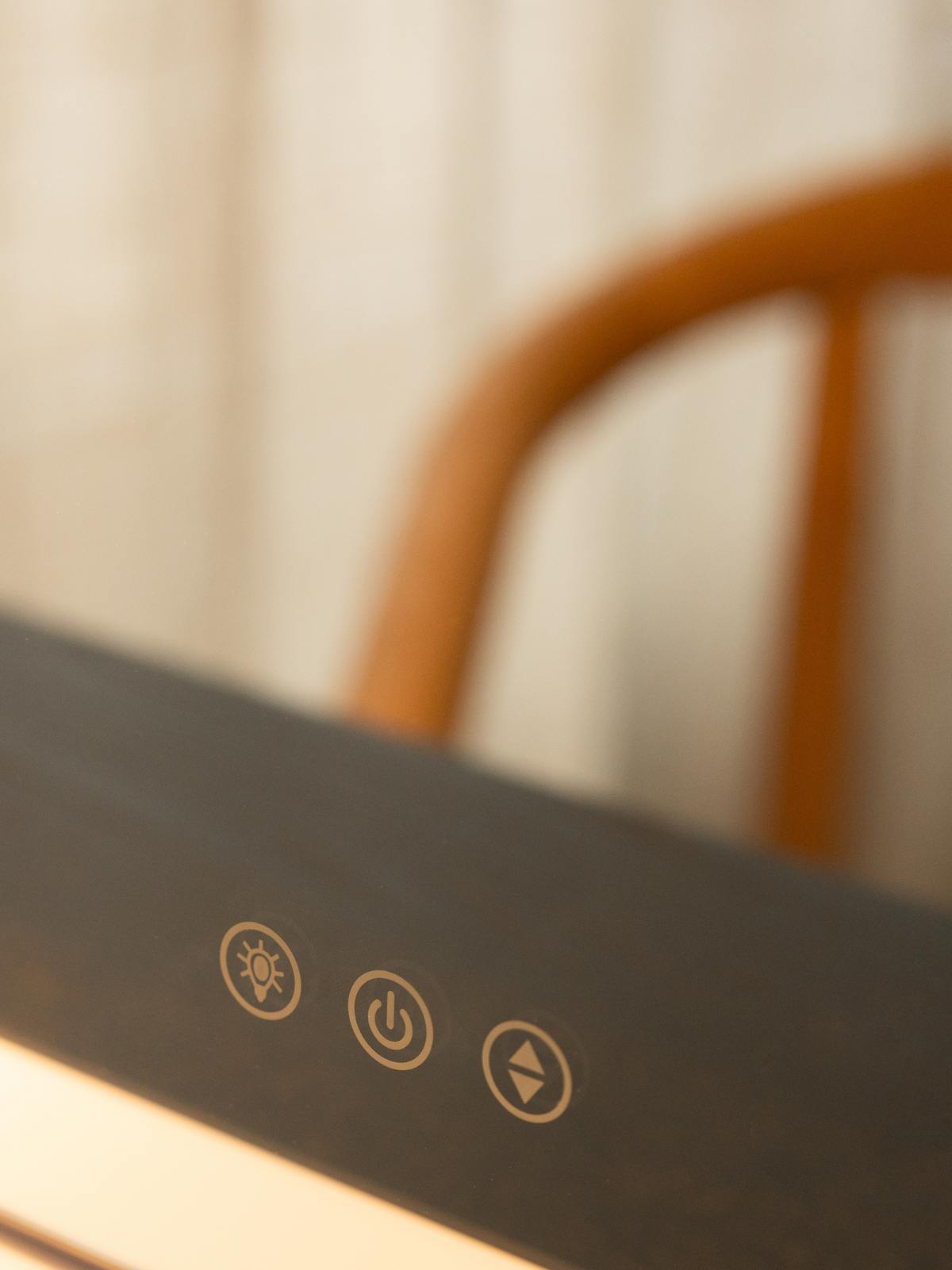 Close-up of dark grey control panel showing three gold touch icons: brightness, power, and colour temperature adjustment
