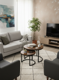 Brown round nesting tables styled in a living room, larger holding books and mug, smaller with a succulent, black steel ba…