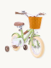 Sage green Luca kids bike angled front-left view, showing wicker basket, cream tyres, brown saddle, and training wheels on…