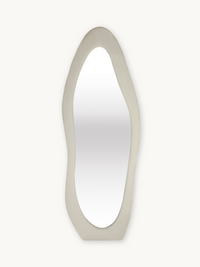 Tall asymmetric standing mirror with wide off-white suede velvet upholstered frame, front view on plain background