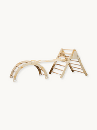 Natural wood Pikler-style 3-piece climbing set showing triangle frame, rocker arch, and ramp connected together, angled pr…