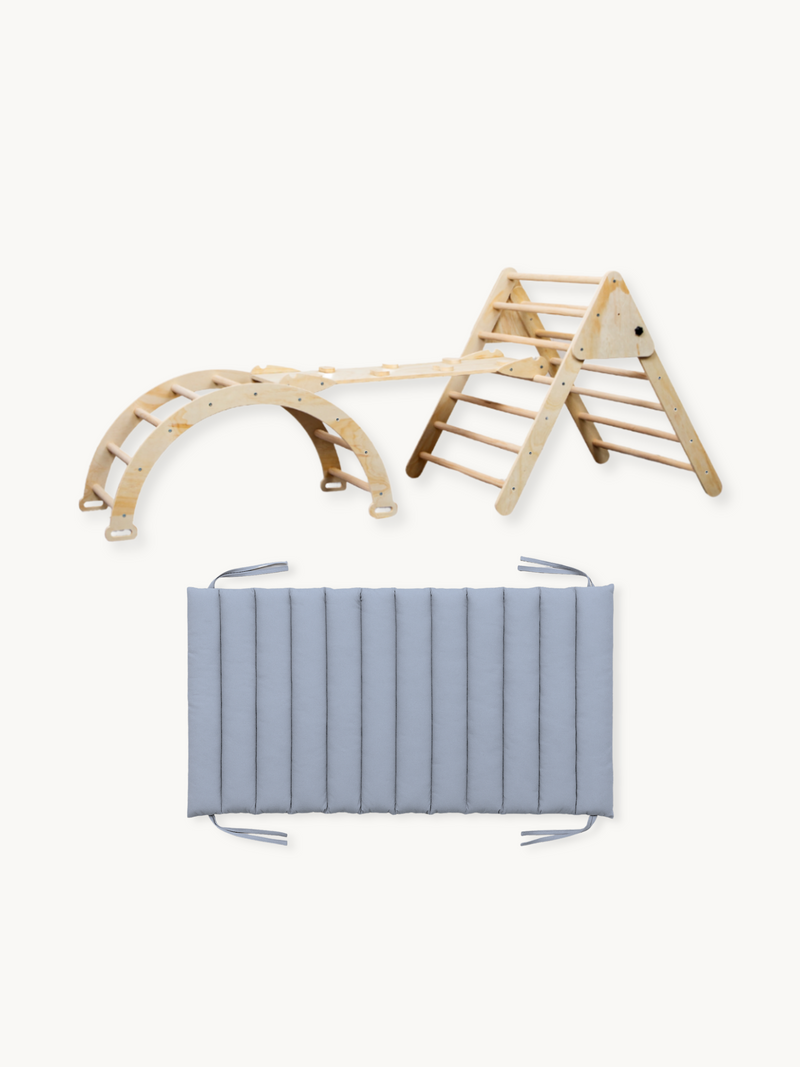 Natural wood Pikler climbing triangle, arch, and ramp set shown assembled beside a flat gray channel-stitched cushion with…